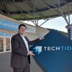 Christoph Rothe zeigt das TechTide-Schild am Eingang des Convention Centers