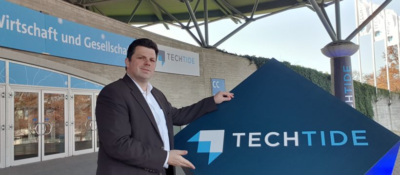 Christoph Rothe zeigt das TechTide-Schild am Eingang des Convention Centers