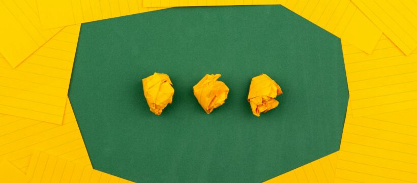 three crumpled yellow papers on green surface surrounded by yellow lined papers