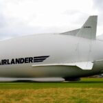A large Airlander hybrid airship parked on a grassy field under a cloudy sky.