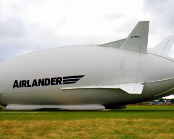 A large Airlander hybrid airship parked on a grassy field under a cloudy sky.