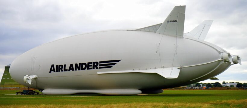 A large Airlander hybrid airship parked on a grassy field under a cloudy sky.